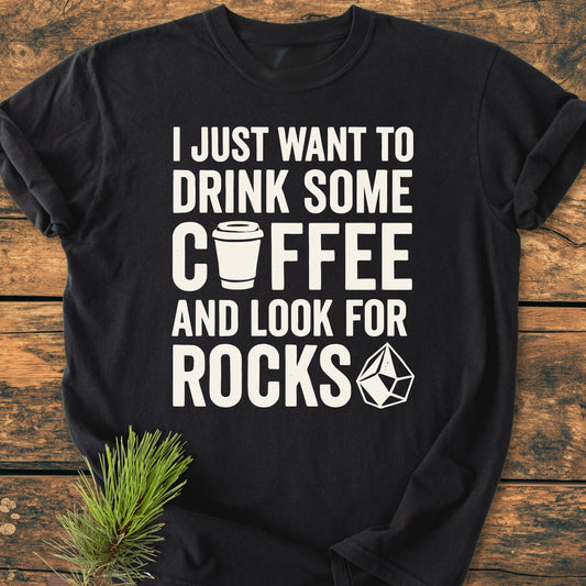 Black T-shirt titled 1404 Drink Coffee And Look For Rocks Base with bold white lettering and icons, styled with a pine sprig. Made of 100% ring-spun cotton, offering a relaxed fit.