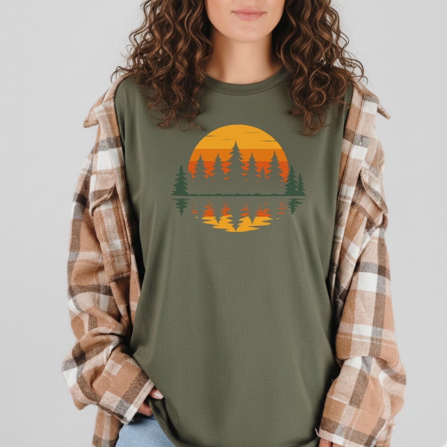 Person wearing Retro Sunset Pines T-Shirt with pine tree silhouette graphic under a plaid flannel jacket, embodying outdoor adventure spirit and comfort.
