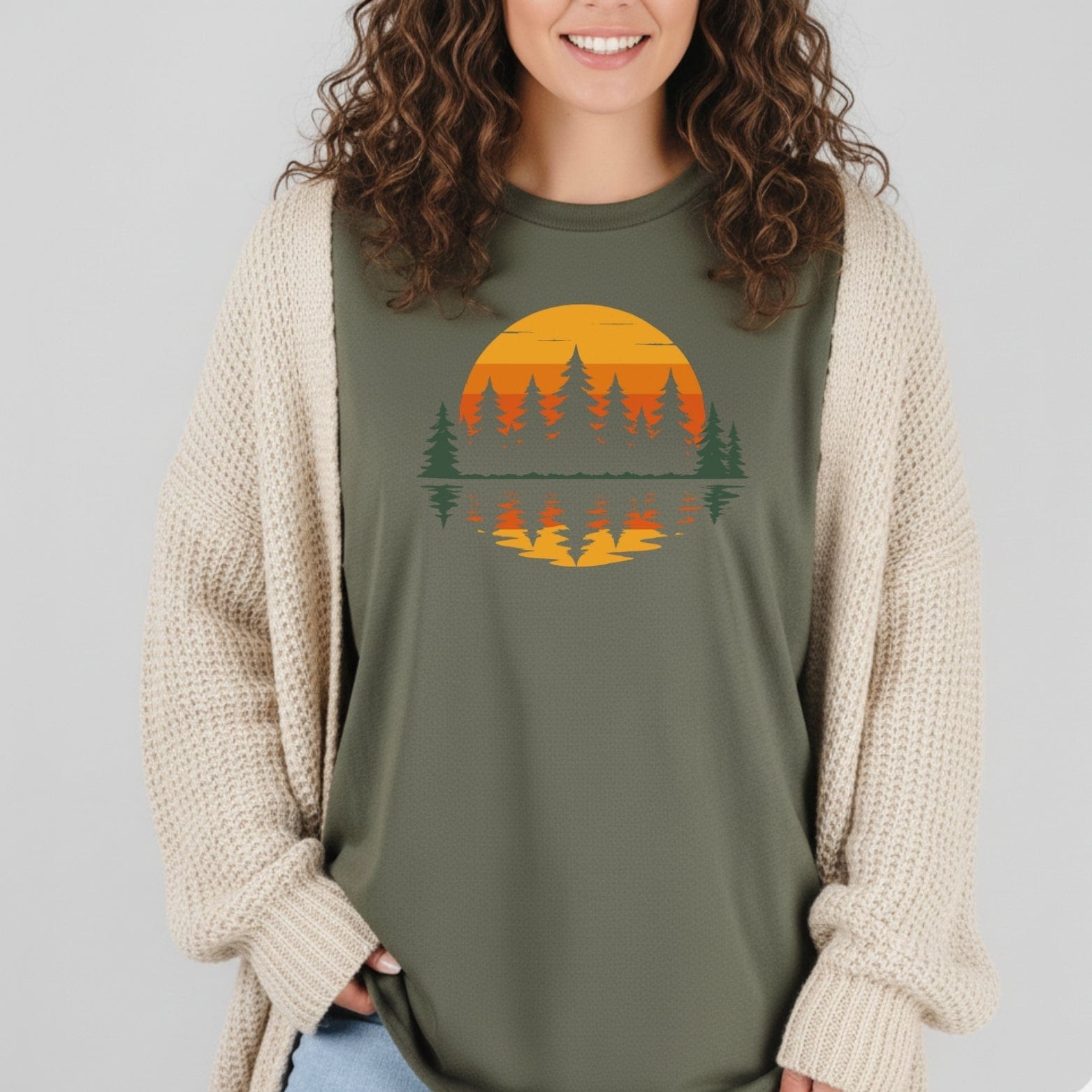 Retro Sunset Pines T-Shirt with a sunset and pine tree design, worn under a cream knit cardigan, showcasing outdoor-inspired style and comfort.