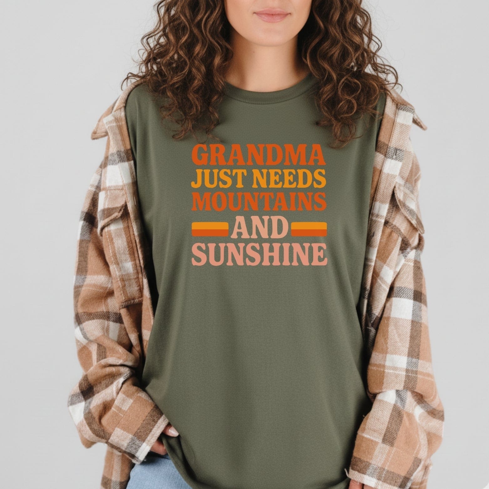 Retro 80s Grandma Mountains T-Shirt with bold lettering, layered under a plaid overshirt, showcasing a love for outdoor adventures and timeless comfort.