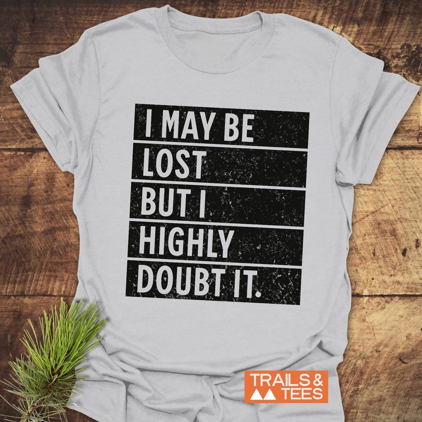 Close-up of the I May Be Lost But I Highly Doubt It T-shirt, featuring bold text, displayed alongside a black and white sign.