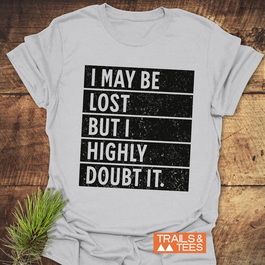 Close-up of the I May Be Lost But I Highly Doubt It T-shirt, featuring bold text, displayed alongside a black and white sign.