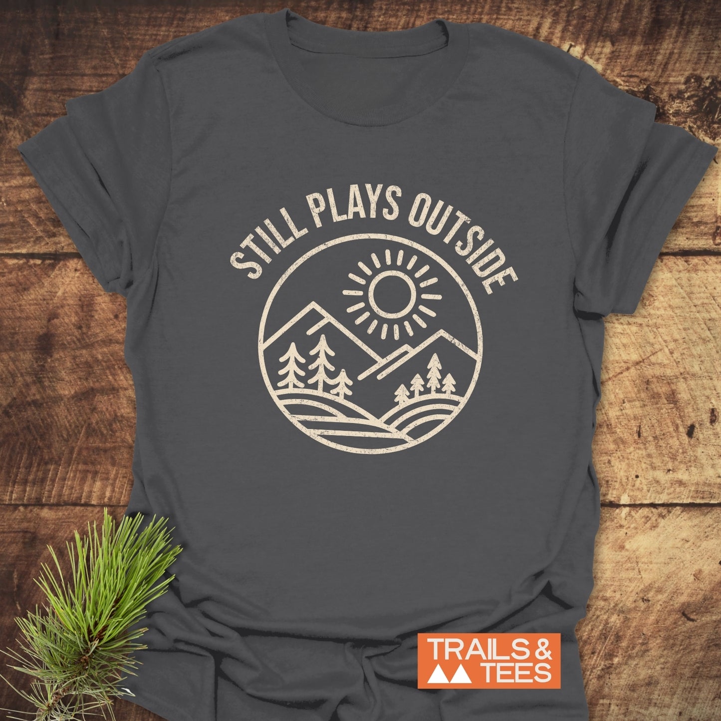 Still Plays Outside T-Shirt featuring durable white text on a grey background, crafted from soft ring-spun cotton for comfort and adventure-ready durability.