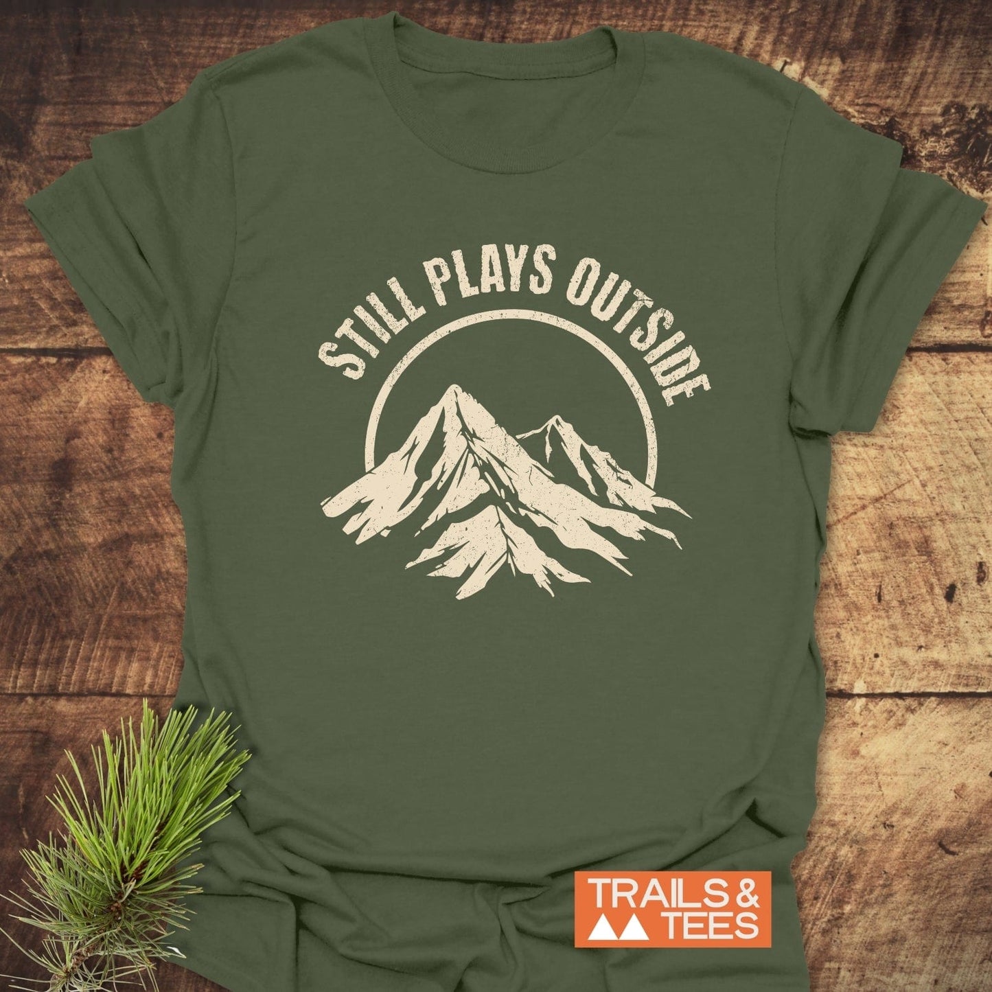 Still Plays Outside T-Shirt featuring a mountain logo and white text, crafted from soft ring-spun cotton for everyday outdoor adventures.