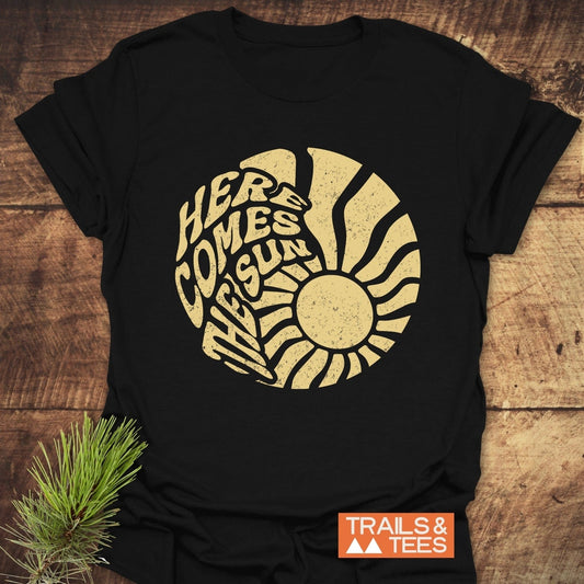 Here Comes The Sun T-Shirt featuring durable yellow text on soft, black ring-spun cotton, designed for comfort and adventure, perfect for outdoor enthusiasts.