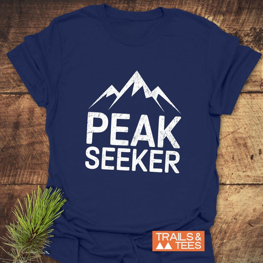 Navy-blue Peak Seeker T-shirt with mountain graphic, styled with pine sprig. Made from soft ring-spun cotton. Features durable prints and taped shoulders.