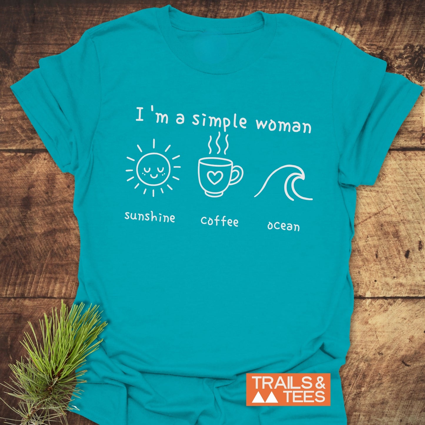 Turquoise-blue I'm A Simple Woman - Sunshine Coffee Ocean T-shirt with hand-lettered design and icons, laid on wood, featuring TRAILS & TEES logo.