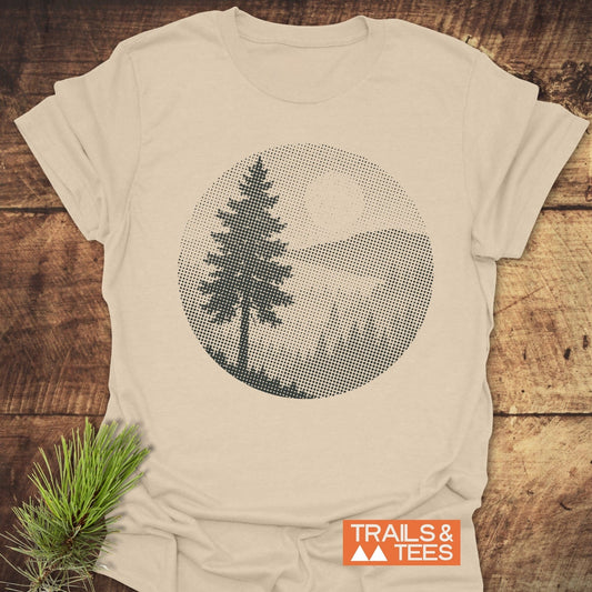 Sunset Woods Halftone T-Shirt featuring a pine tree and mountain graphic, laid on wood. Showcases outdoor-themed design with durable, pre-shrunk cotton for comfort.