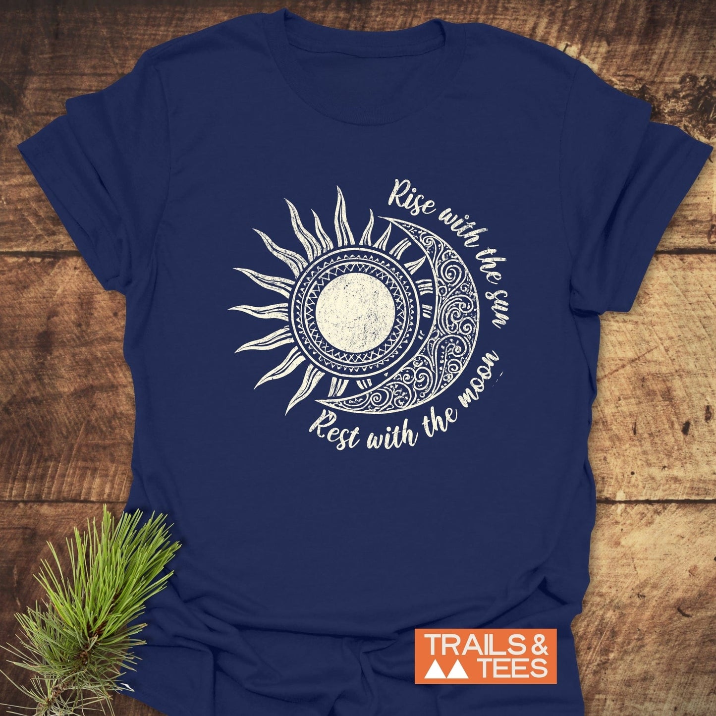 Sun & Moon Mystical Boho T-Shirt with a half-sun/half-moon graphic and slogan, Rise with the sun – Rest with the moon, beside a pine sprig.