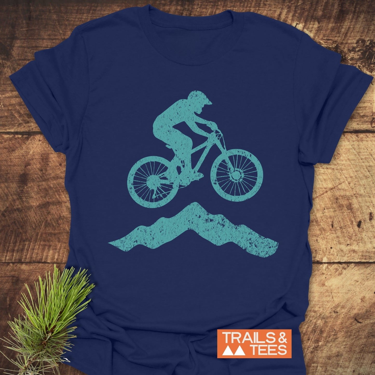 Airborne Mountainbiker T-Shirt on rustic surface, featuring a teal mountain biker graphic. Comfortable, pre-shrunk navy tee ideal for outdoor enthusiasts.