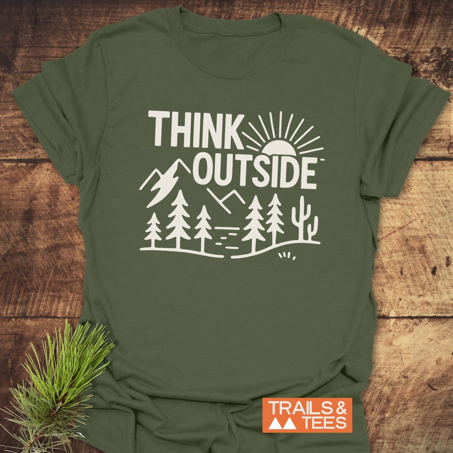 Think Outside Hiking T-Shirt with bold slogan and nature scene, featuring mountains, sun, and trees; includes orange TRAILS & TEES tag, highlighting outdoor-ready design.