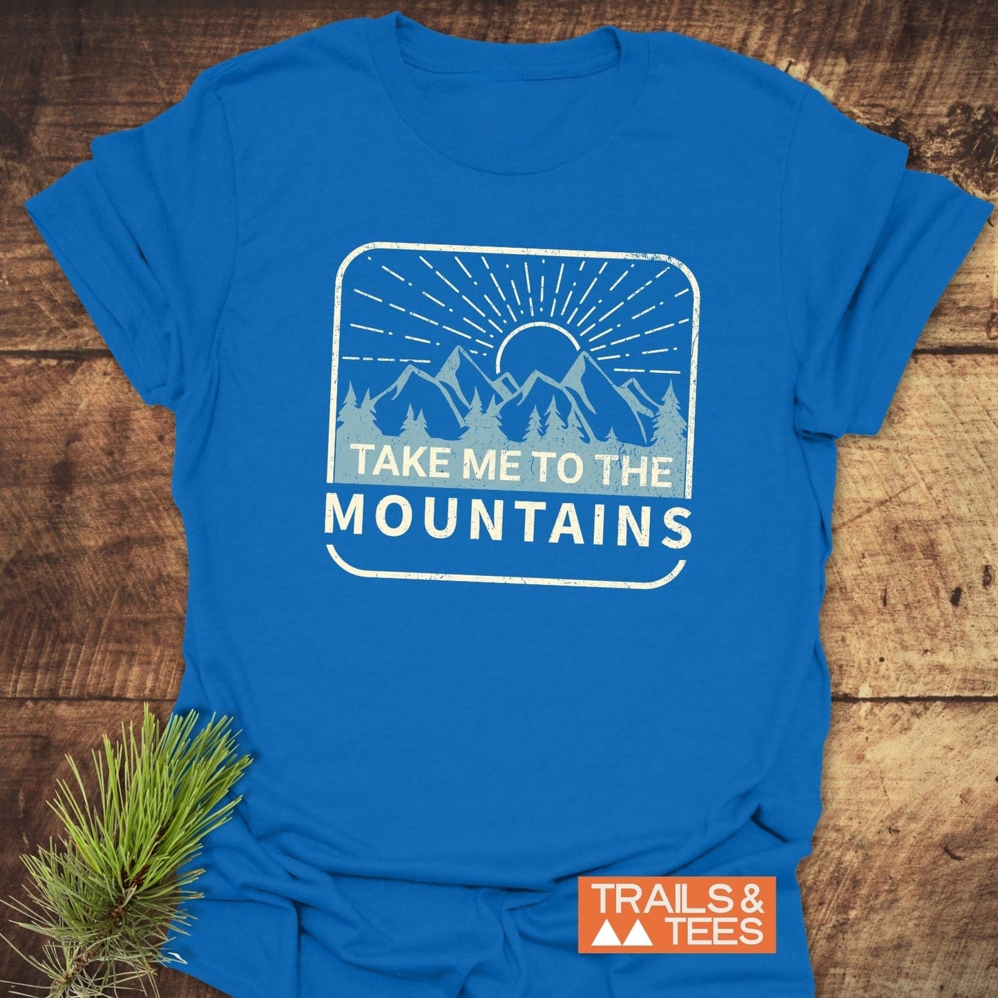 Take Me To The Mountains T-Shirt featuring a weathered mountain graphic and slogan. Crafted from soft, lightweight cotton for outdoor enthusiasts.