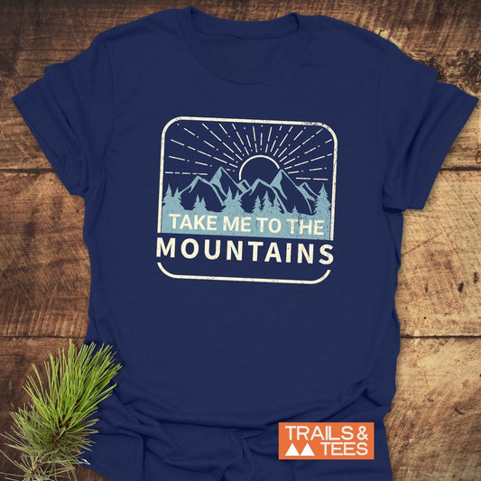 Take Me To The Mountains T-Shirt showcasing a mountain scene with slogan, crafted from soft cotton for adventure and comfort, featuring durable prints and sustainable production.