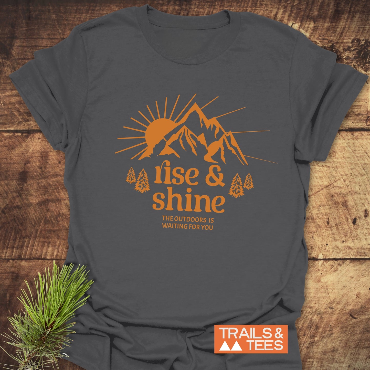 Rise And Shine T-Shirt featuring a sunrise and mountain design in orange, symbolizing outdoor adventure, on soft, durable, ring-spun cotton.