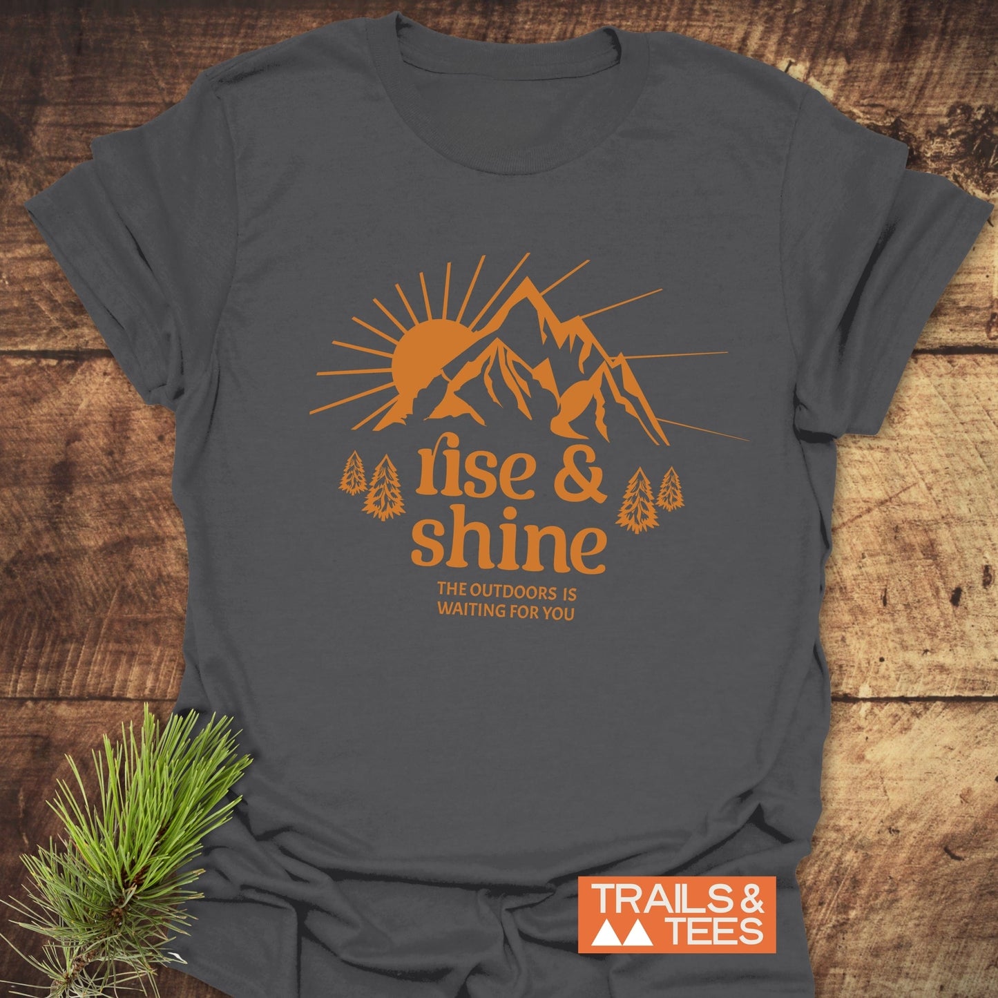 Rise And Shine T-Shirt featuring a sunrise and mountain design in orange, symbolizing outdoor adventure, on soft, durable, ring-spun cotton.