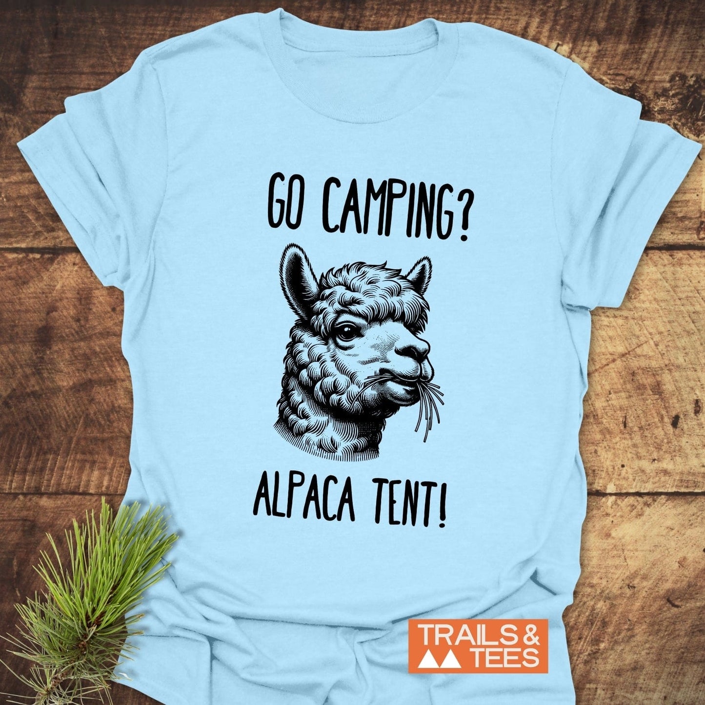 Go Camping? Alpaca Shirt! T-Shirt featuring an alpaca print with a playful caption, laid on wood with pine sprig, embodying outdoor adventure.