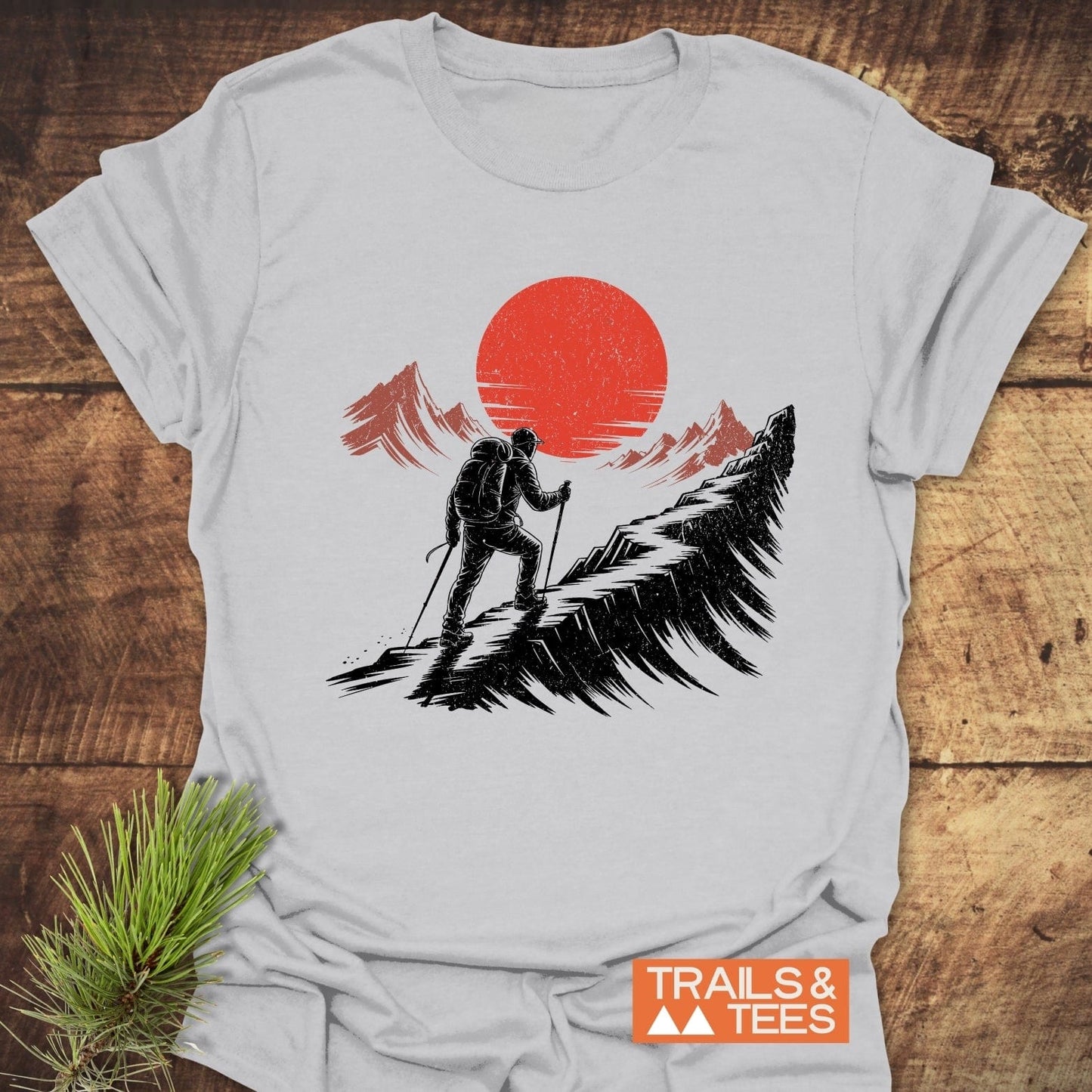 Hiker Sunset T-Shirt featuring a black hiker silhouette against a red sun, crafted from soft, lightweight cotton for comfort and durability. Includes TRAILS & TEES logo.