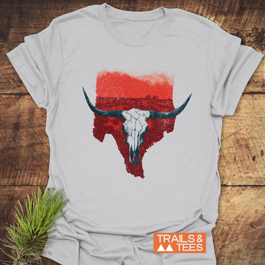 Hike Texas T-Shirt featuring a distressed Texas silhouette with a longhorn skull, laid on wood, showcasing Trails & Tees logo and pine sprig.