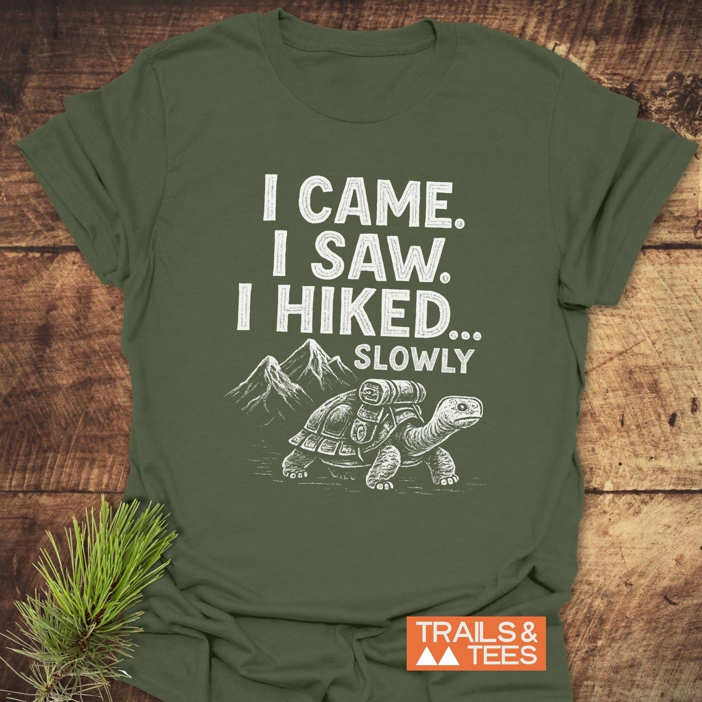 I Came, I Saw T-Shirt: Olive-green shirt with tortoise graphic, hiking text, styled with pine sprig. Comfortable, durable, adventure-ready design.