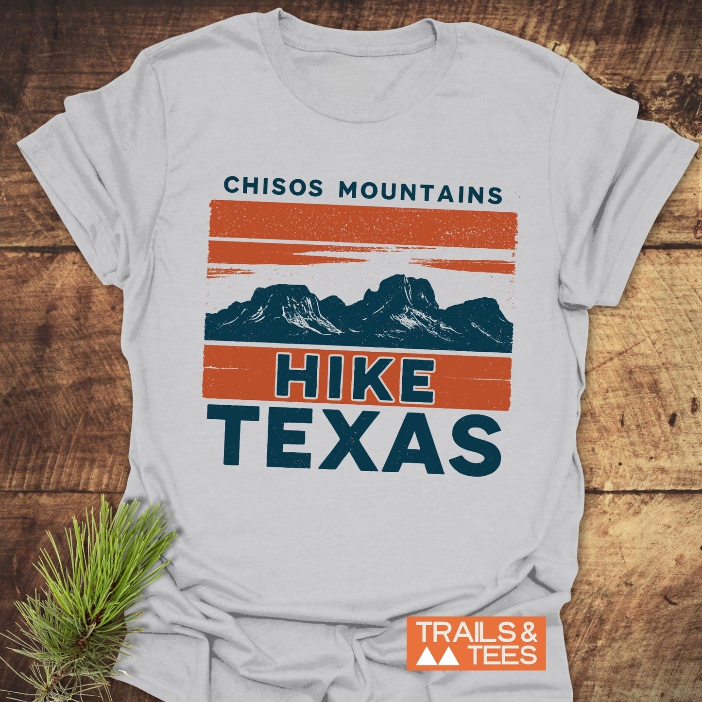 Chisos Mountains Texas T-Shirt featuring a bold mountain graphic, styled on rustic wood with a pine sprig, crafted from soft, durable ring-spun cotton.