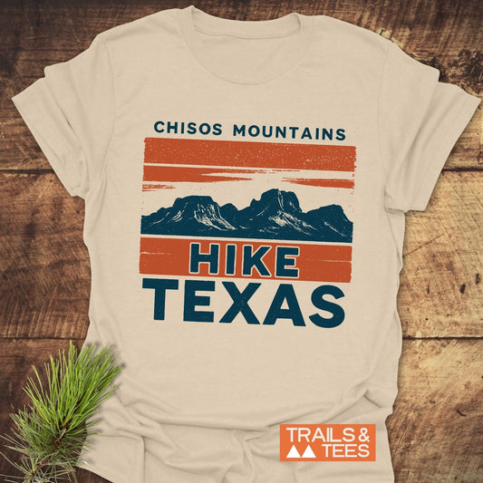 Chisos Mountains Texas T-Shirt with vintage graphic of mountains and stripes, laid on wood. Soft cotton, pre-shrunk, durable print. Pine sprig beside.