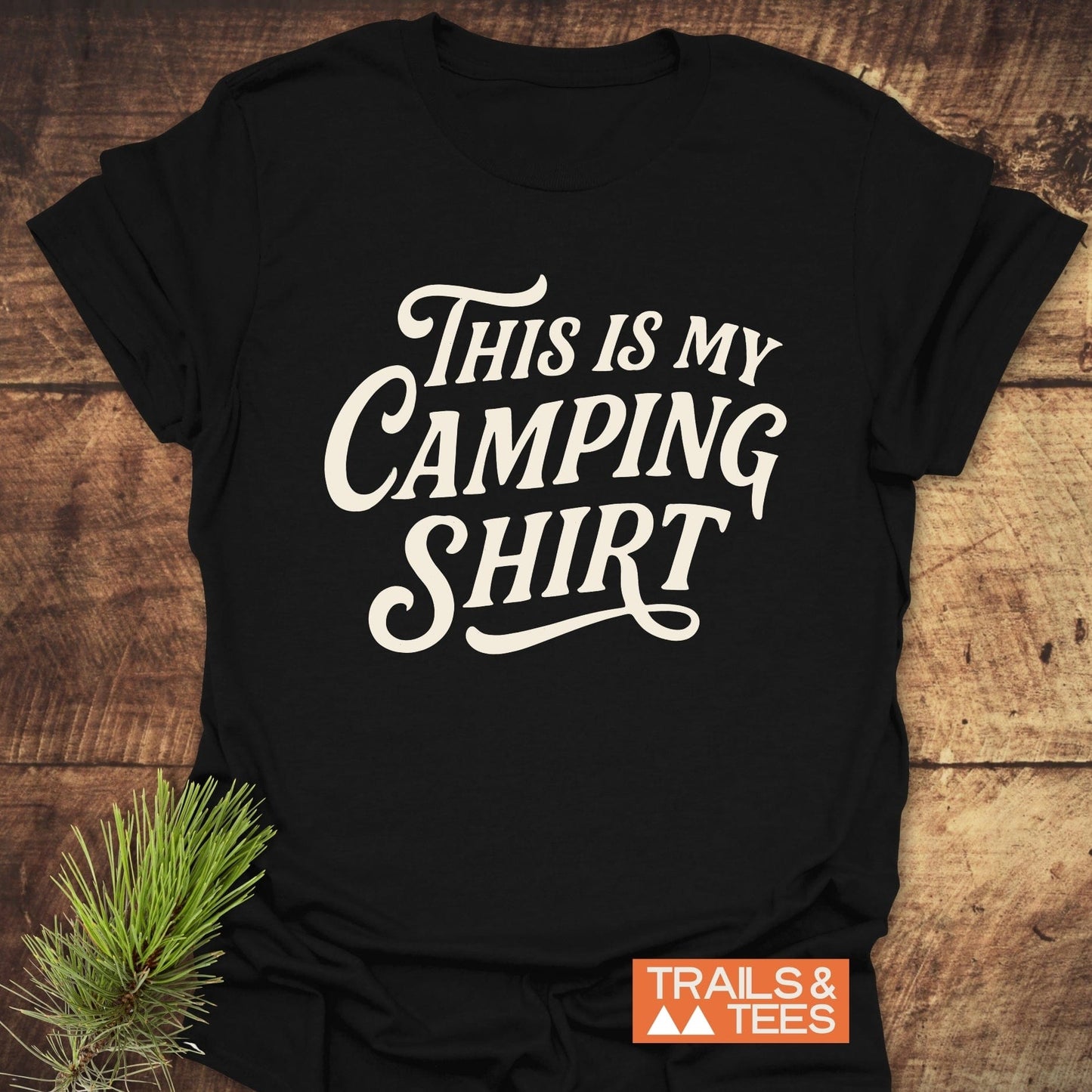 Black T-shirt with This Is My Camping Shirt slogan, showcasing outdoor vibe; pine sprig suggests nature theme. Part of Trails & Tees collection.