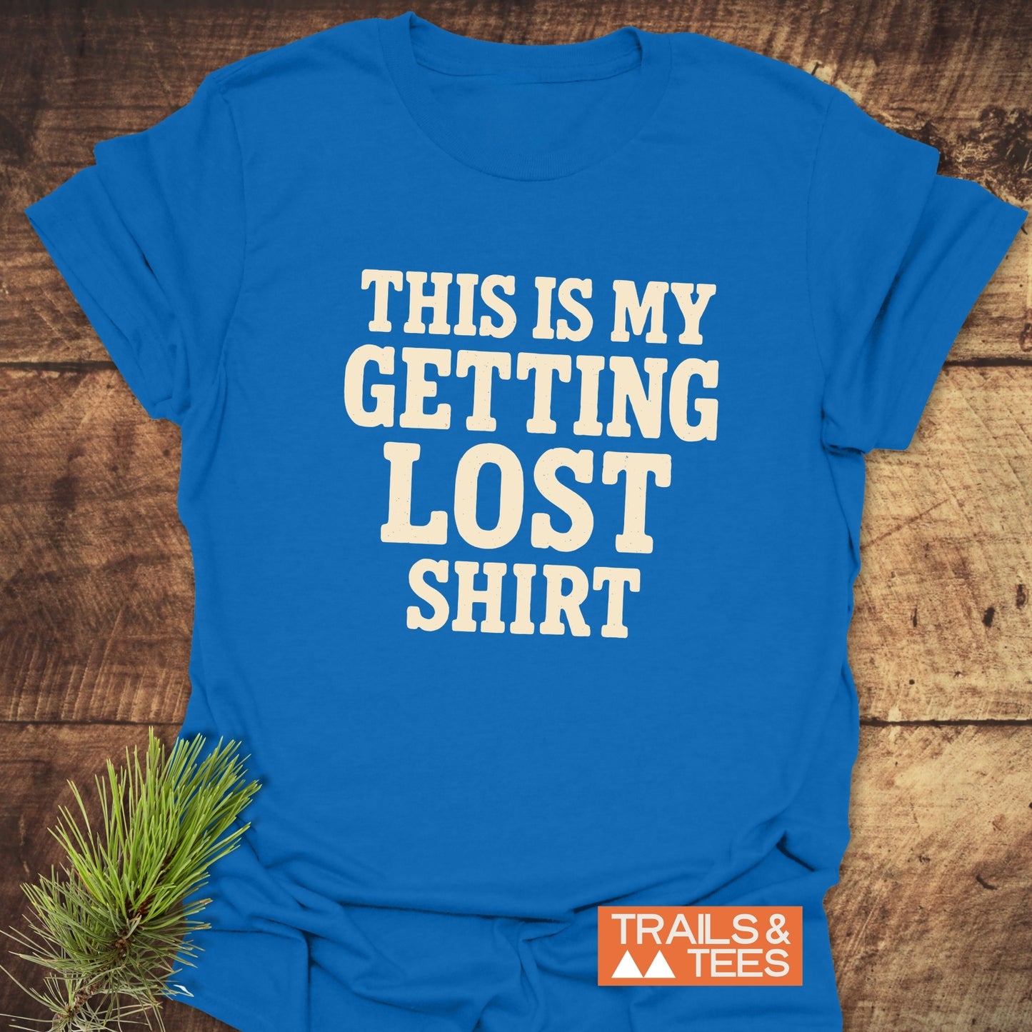 This Is My Getting Lost T-Shirt flat-lay on wood, featuring cream text, orange Trails & Tees logo. Crafted from soft cotton for outdoor adventures.