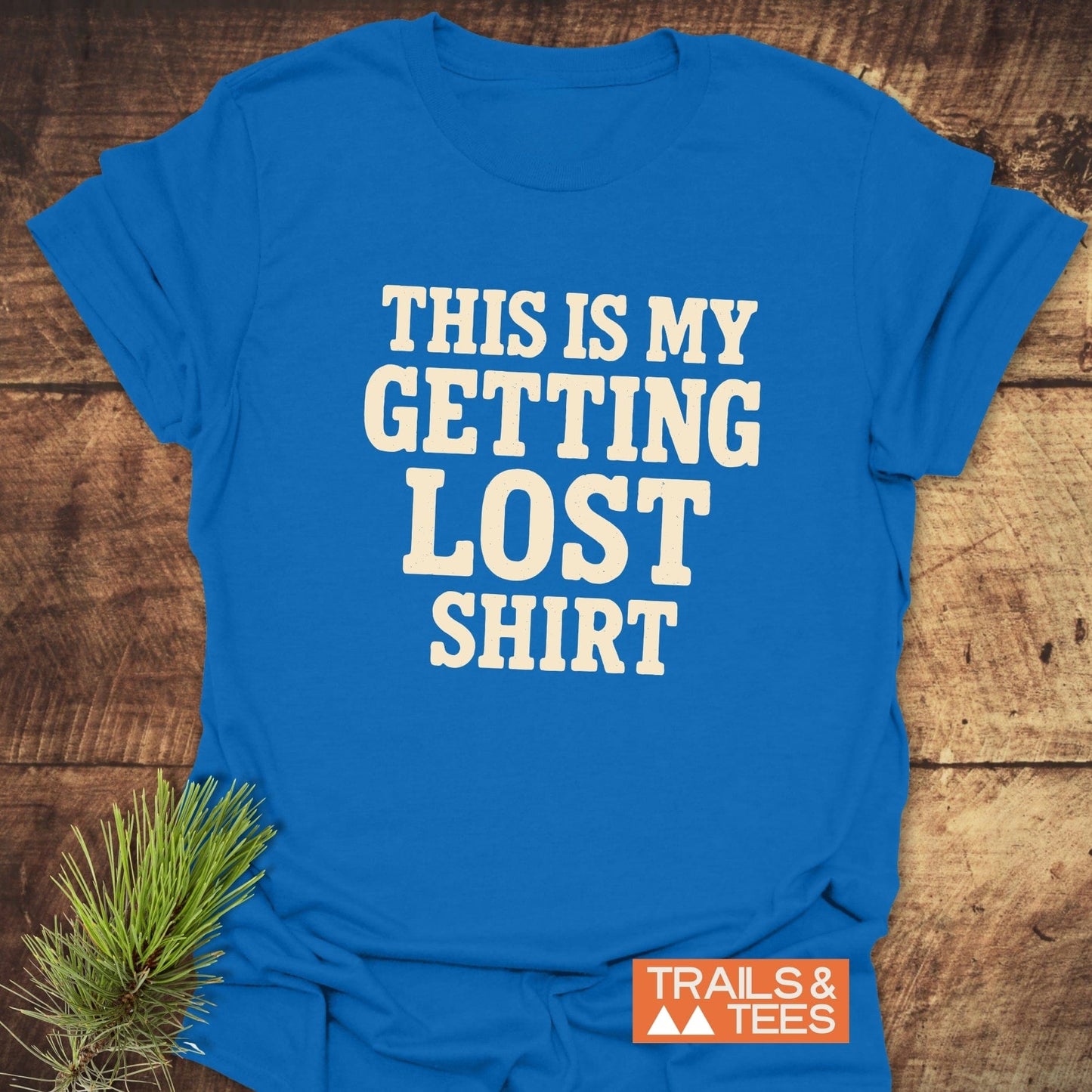 This Is My Getting Lost T-Shirt flat-lay on wood, featuring cream text, orange Trails & Tees logo. Crafted from soft cotton for outdoor adventures.
