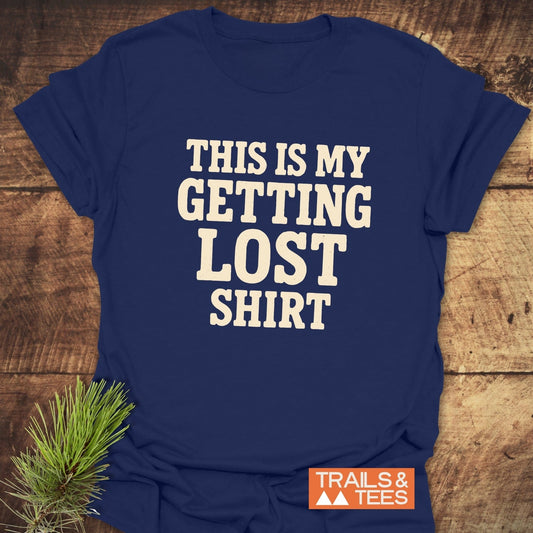This Is My Getting Lost T-Shirt in navy, featuring cream block letters, on a wooden backdrop with a pine sprig, and Trails & Tees logo.