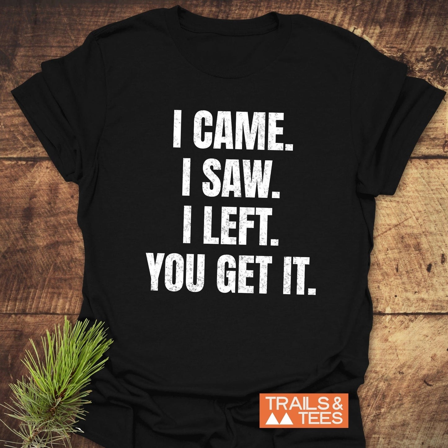 Black I Came. I Saw. I Left. T-shirt on wood, featuring distressed white text. Includes TRAILS & TEES logo, showcasing lightweight, adventure-ready design.