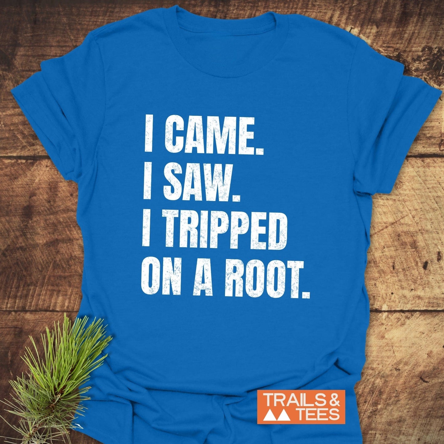 I Came. I Saw. I Tripped... T-Shirt on wood, featuring white distressed text and Trails & Tees logo, with pine branch accentuating outdoor theme.