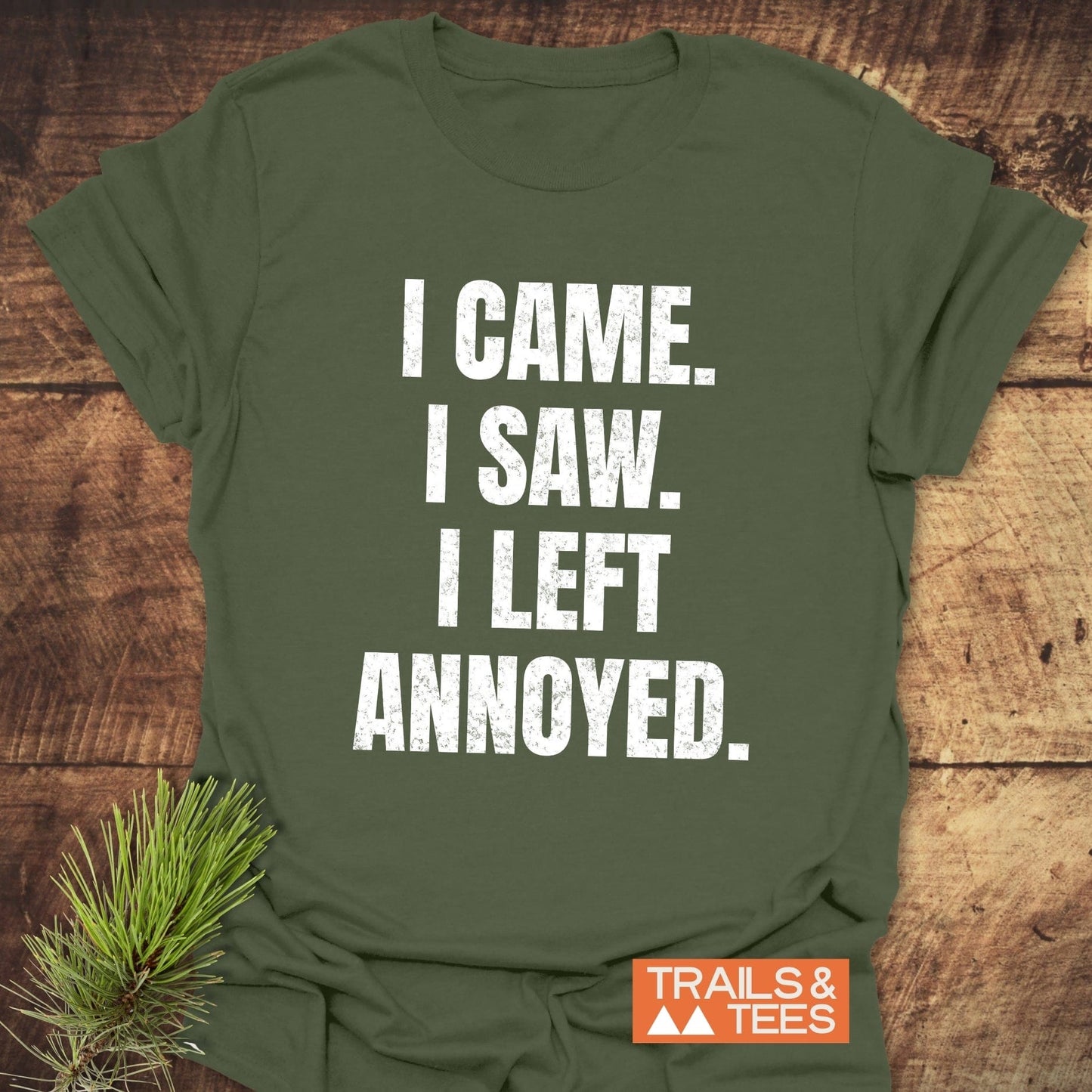 Olive-green I Came. I Saw. Annoyed. T-shirt with distressed white lettering, orange TRAILS & TEES. logo, on rustic wood. Soft, lightweight for outdoor adventures.