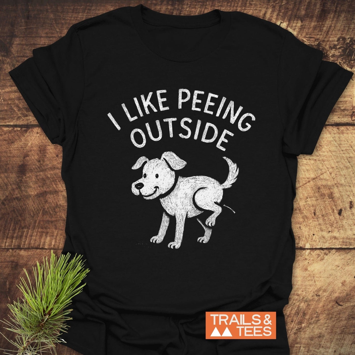 Black T-shirt with I LIKE PEEING OUTSIDE text and dog illustration, featuring a small TRAILS & TEES logo; crafted for outdoor comfort and adventure.
