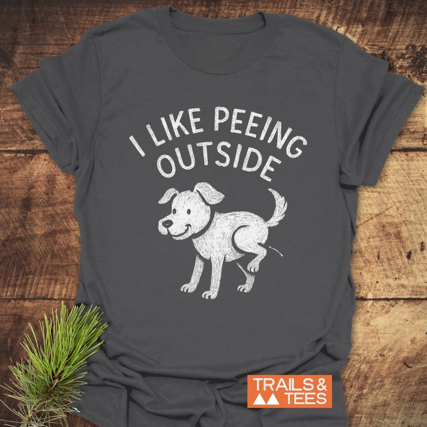 Dark-gray I Like Peeing Outside T-shirt with a white dog illustration, crafted from soft ring-spun cotton, featuring durable prints and an orange TRAILS & TEES logo.