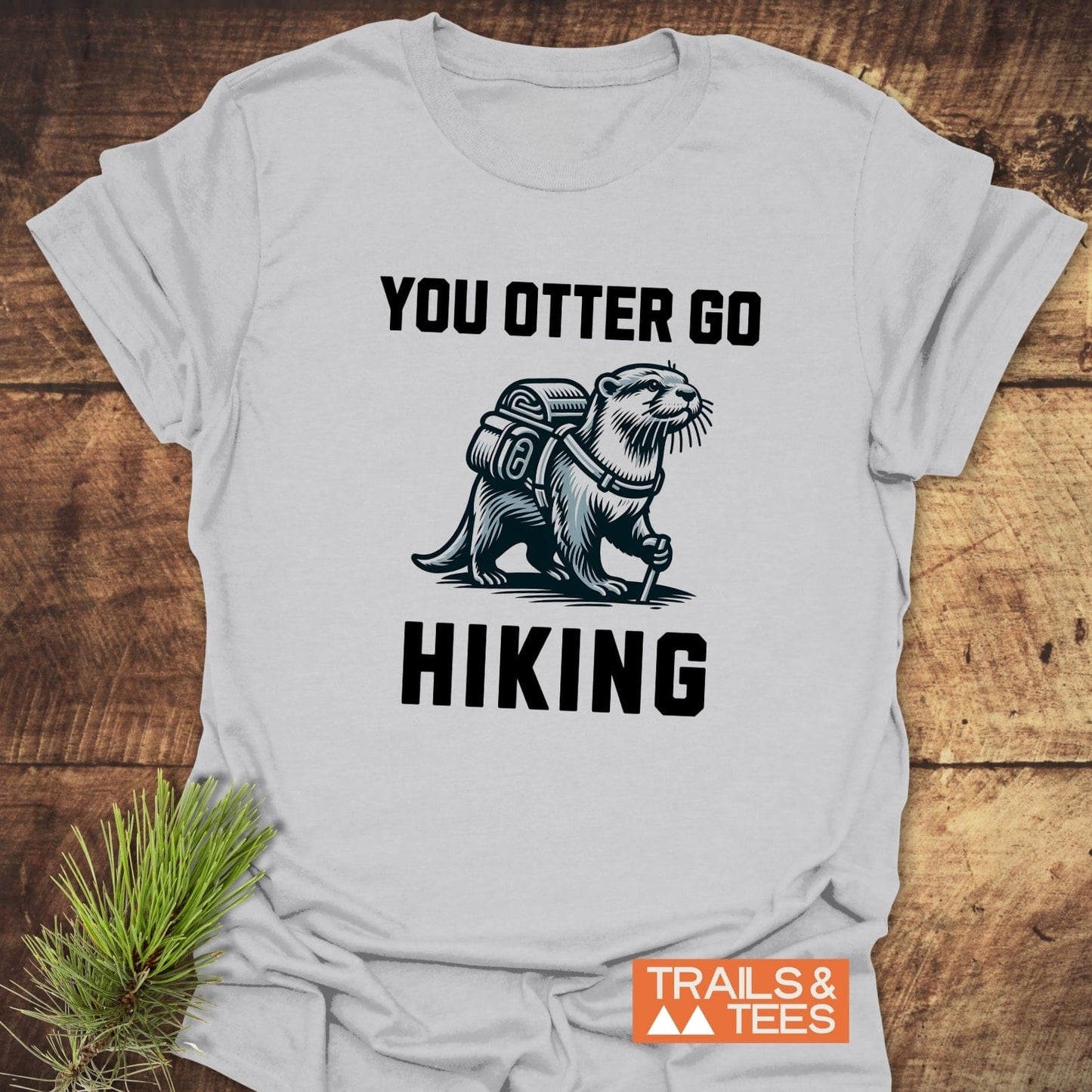 You Otter Go Hiking T-Shirt featuring an otter with backpack illustration, slogan, and Trails & Tees logo, crafted from lightweight cotton for outdoor enthusiasts.