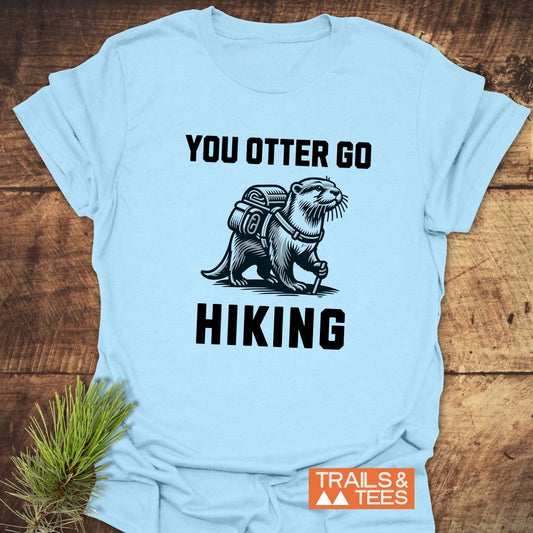 You Otter Go Hiking T-Shirt: Light-blue tee featuring an otter with backpack, hiking pole, and bold slogan, ideal for outdoor enthusiasts.