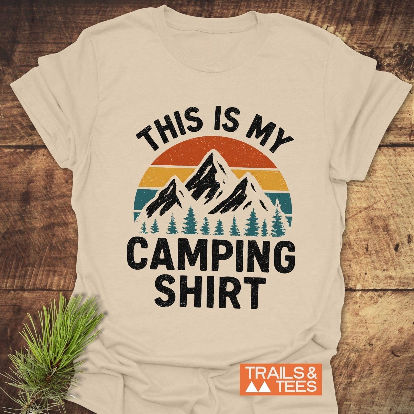Light-beige T-shirt with vintage mountain sunset graphic and THIS IS MY CAMPING SHIRT text, showcasing outdoor-themed design by Trails & Tees.