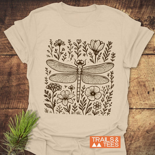 Dragonfly T-Shirt featuring a hand-drawn dragonfly amid wildflowers, laid on wood. Soft, ring-spun cotton, pre-shrunk, durable print, ideal for outdoor enthusiasts.