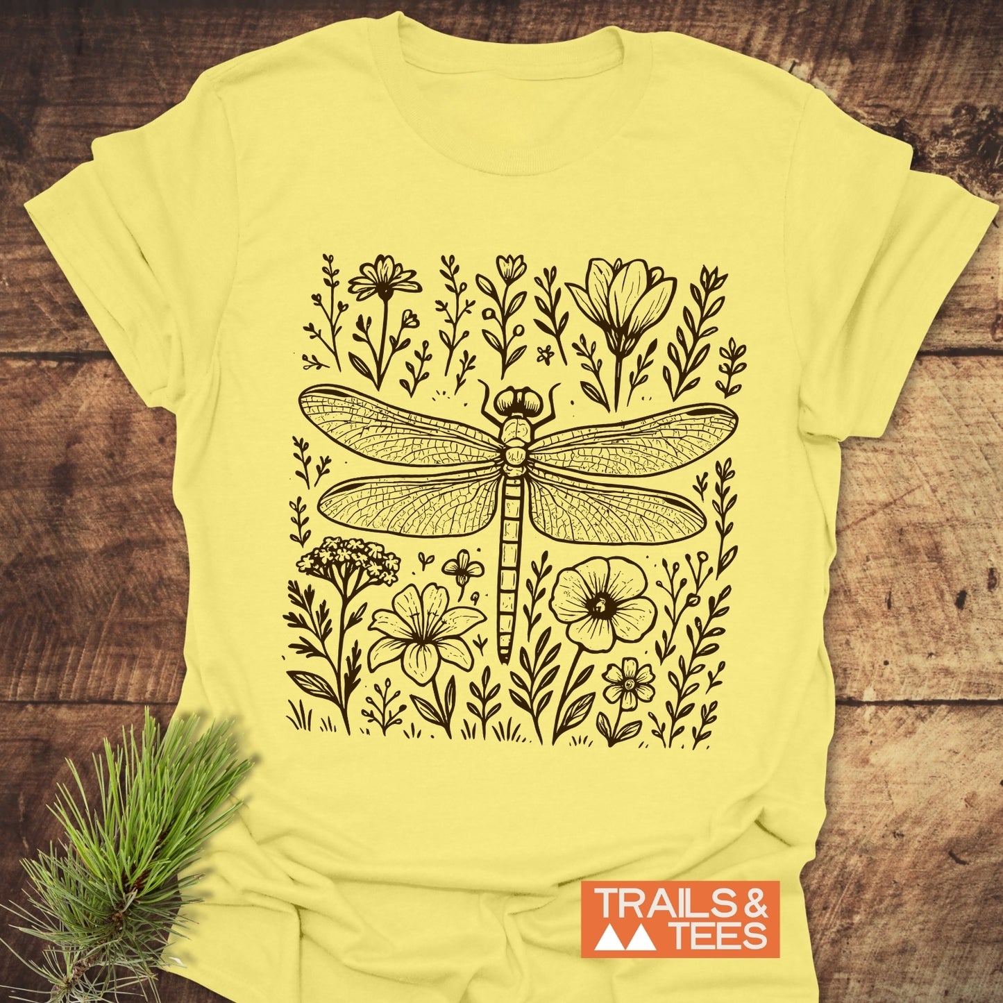 Dragonfly T-Shirt featuring a black-ink dragonfly and meadow flowers on pale-yellow fabric, crafted from soft ring-spun cotton for trail-tested comfort and durability.