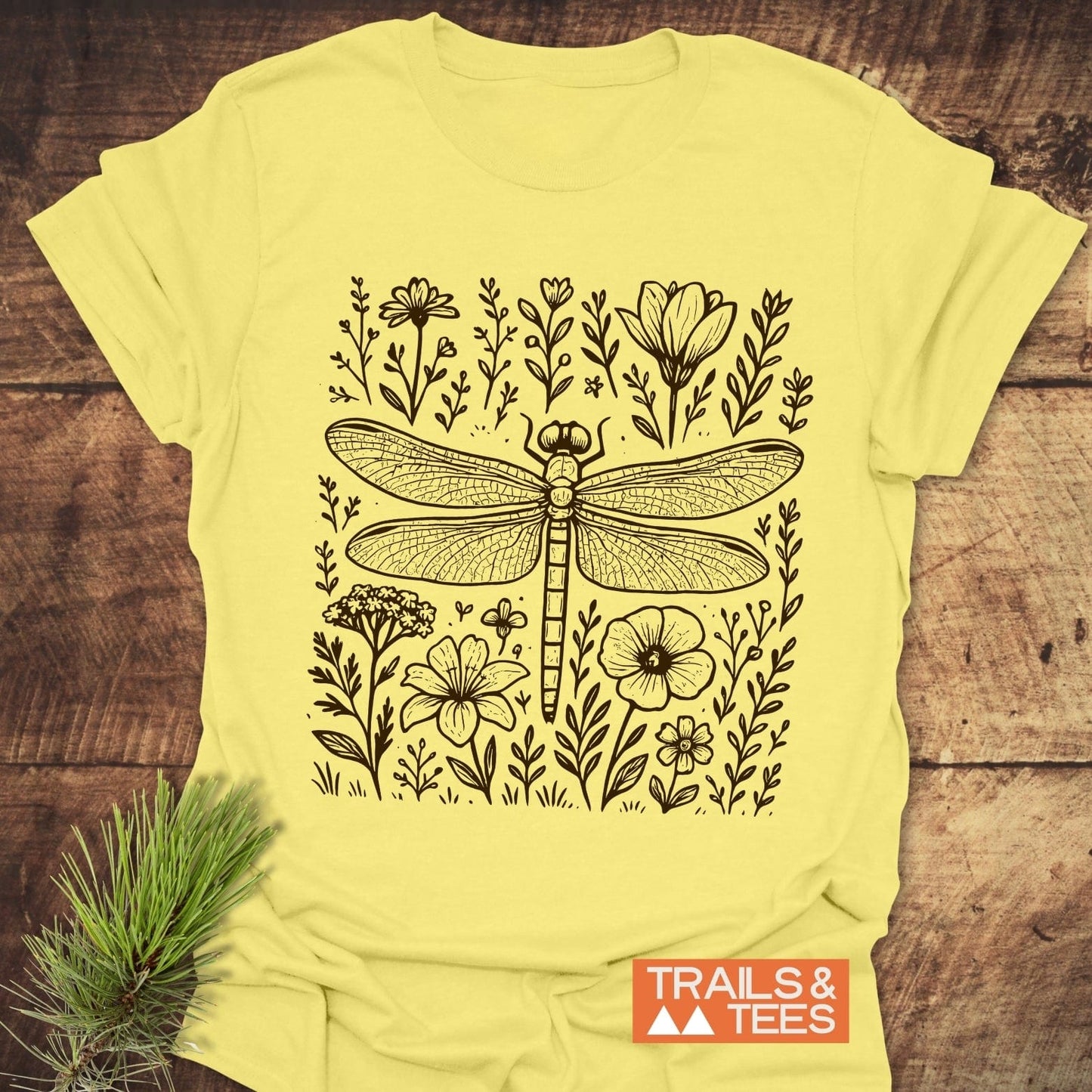 Dragonfly T-Shirt featuring a black-ink dragonfly and meadow flowers on pale-yellow fabric, crafted from soft ring-spun cotton for trail-tested comfort and durability.