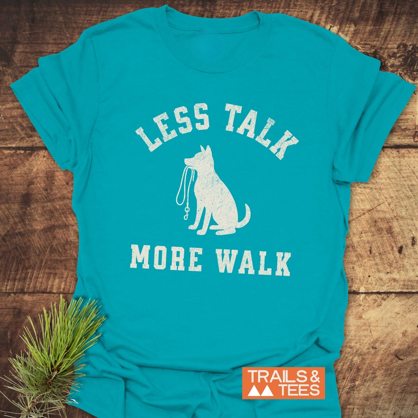 Less Talk, More Walk T-Shirt featuring a seated dog with leash graphic, white “LESS TALK MORE WALK” text, orange “TRAILS & TEES” label on soft cotton.