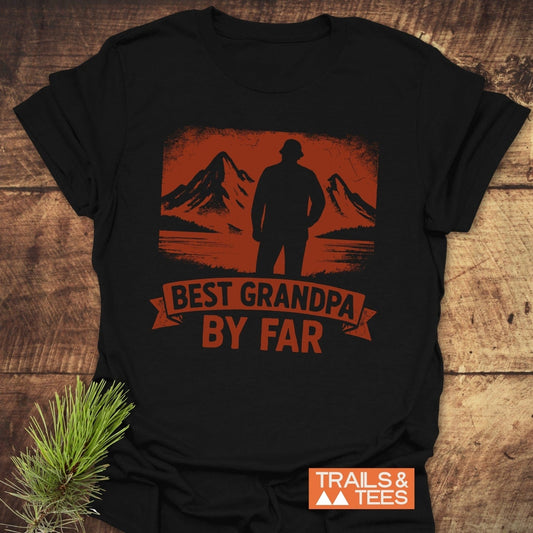 Black T-shirt with mountain-lake graphic and “BEST GRANDPA BY FAR” slogan, showcasing outdoor spirit. Brand “TRAILS & TEES” logo visible.
