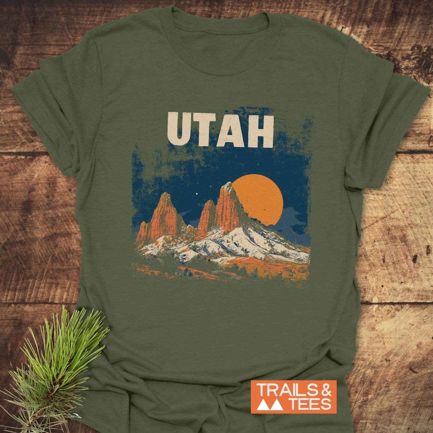 Utah Retro T-Shirt featuring red rock formations and sun graphic on olive-green fabric, laid flat on rustic wood, ideal for outdoor enthusiasts.
