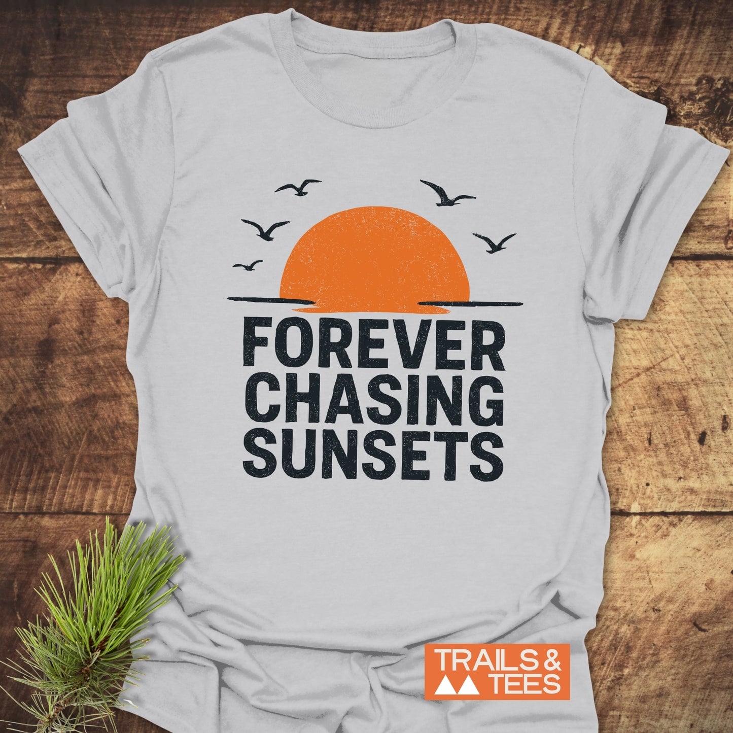 Forever Chasing Sunsets T-Shirt featuring an orange half-sun and bird silhouettes. Made of soft, lightweight cotton for everyday outdoor adventures.