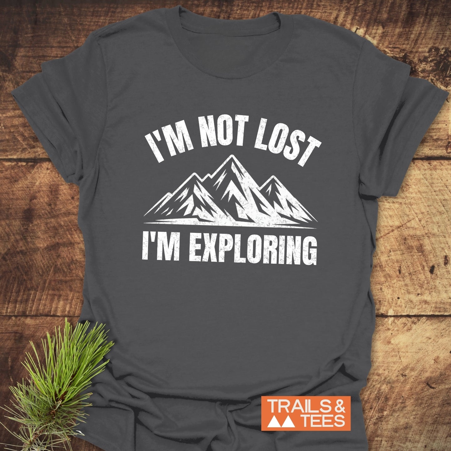 Charcoal-gray T-shirt featuring a distressed white graphic of mountains with I'M NOT LOST, I'M EXPLORING, highlighting adventure-ready design and comfort.