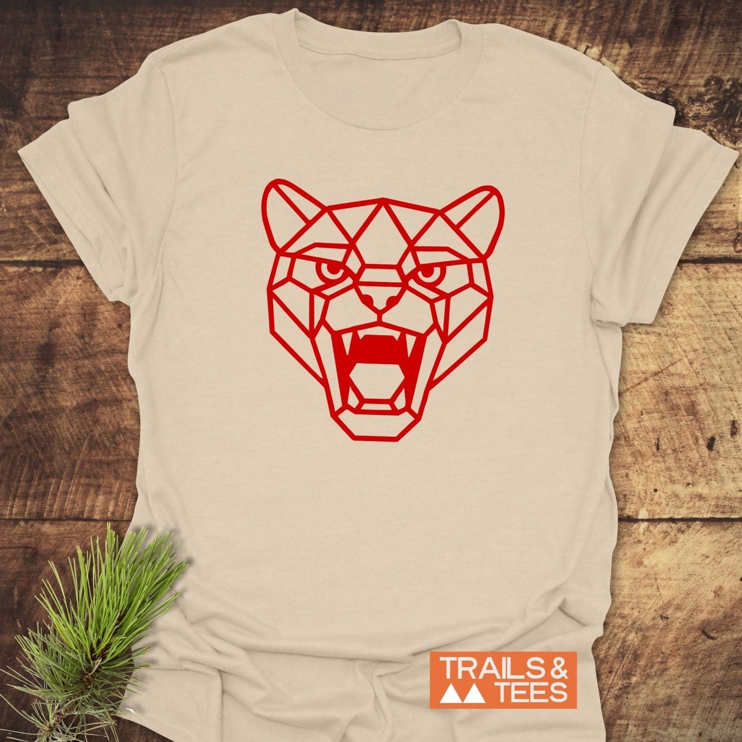 Light-beige Geometric Cougar T-Shirt with a bold red big-cat illustration, crafted from soft, lightweight cotton, laid flat on a wood-plank surface.