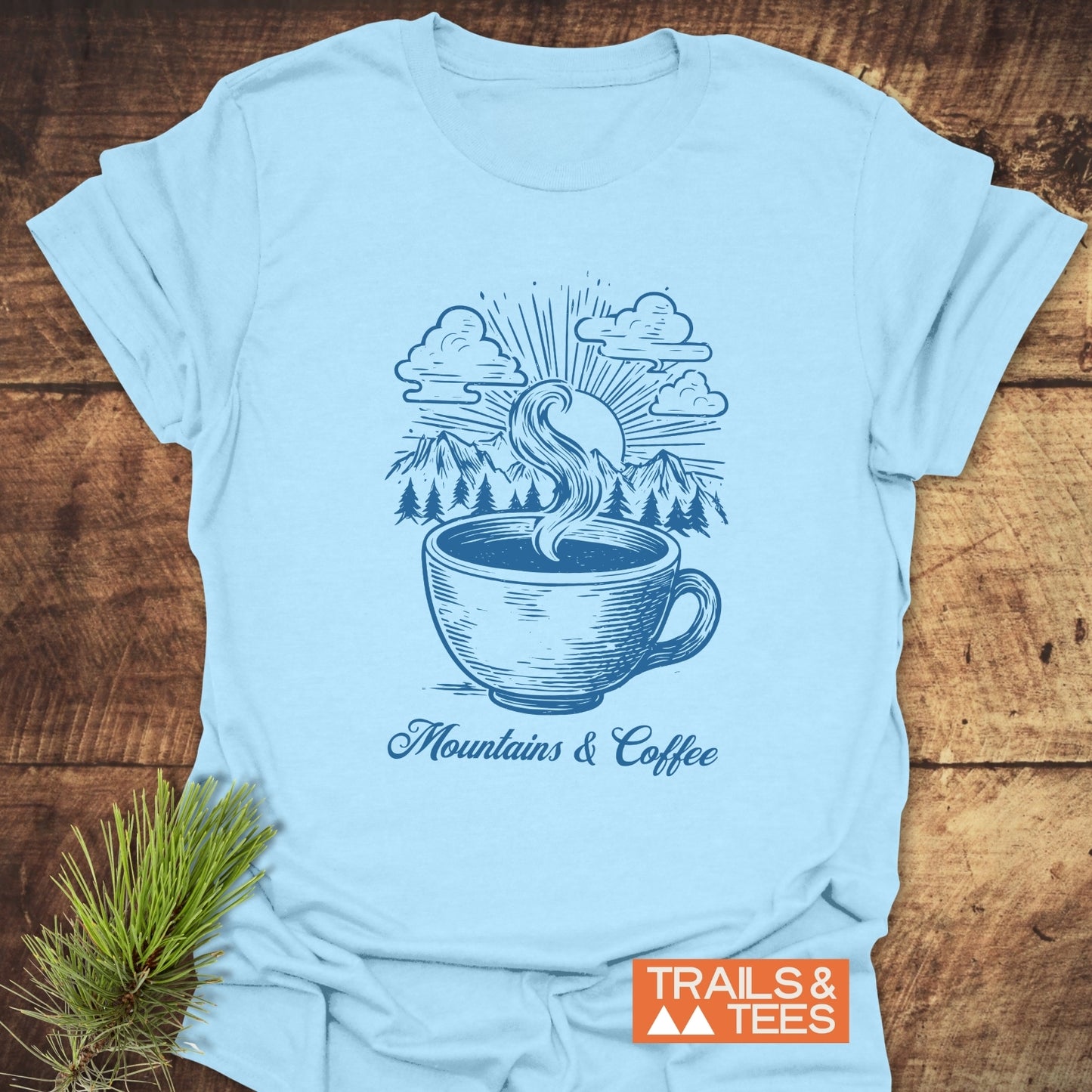 Mountains And Coffee T-Shirt featuring a stylized coffee cup design with mountains and sunburst, promoting outdoor adventure and comfort.