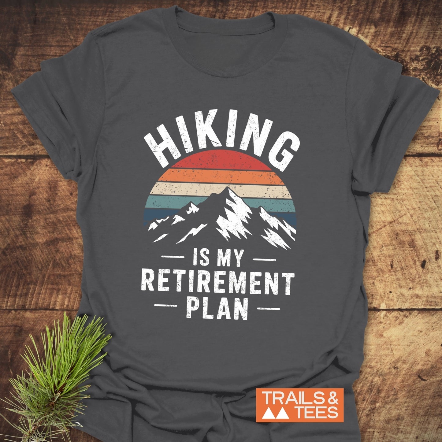 Hiking Is My Retirement Plan T-Shirt featuring a mountain silhouette and sunset stripes, emphasizing outdoor adventure spirit with durable prints and a soft, comfortable fit.