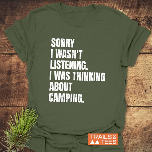 Sorry I Wasn't Listening Camping T-Shirt, olive-green, flat-laid with a pine sprig, features white distressed lettering, crafted from soft ring-spun cotton for outdoor enthusiasts.