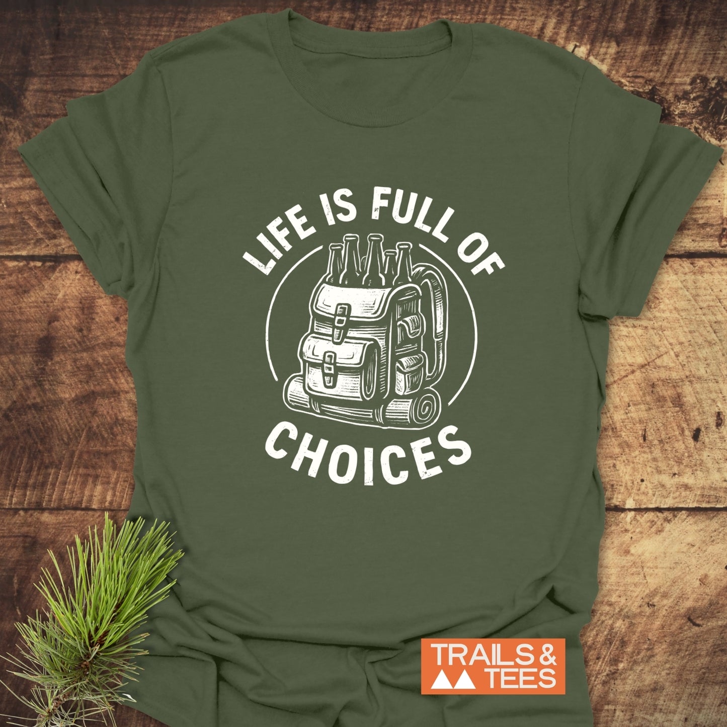 Life Is Full Of Choices T-Shirt featuring a hiking backpack design, laid flat with a pine sprig; embodies adventure-ready, durable cotton comfort.